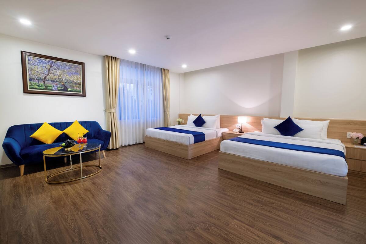 A hotel room with two beds, a sofa, a coffee table, and a painting on the wall.