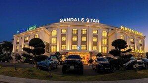 A hotel named 'Sandals Star' with a prominent 'GRASLAND' sign, a 'NAMABANK' sign, and several parked vehicles in front. - Sandals Star Hotel (Duc Trong)