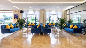 A modern lobby with blue sofas and yellow pillows, large windows, and a polished marble floor. - Sandals Star Hotel (Duc Trong)