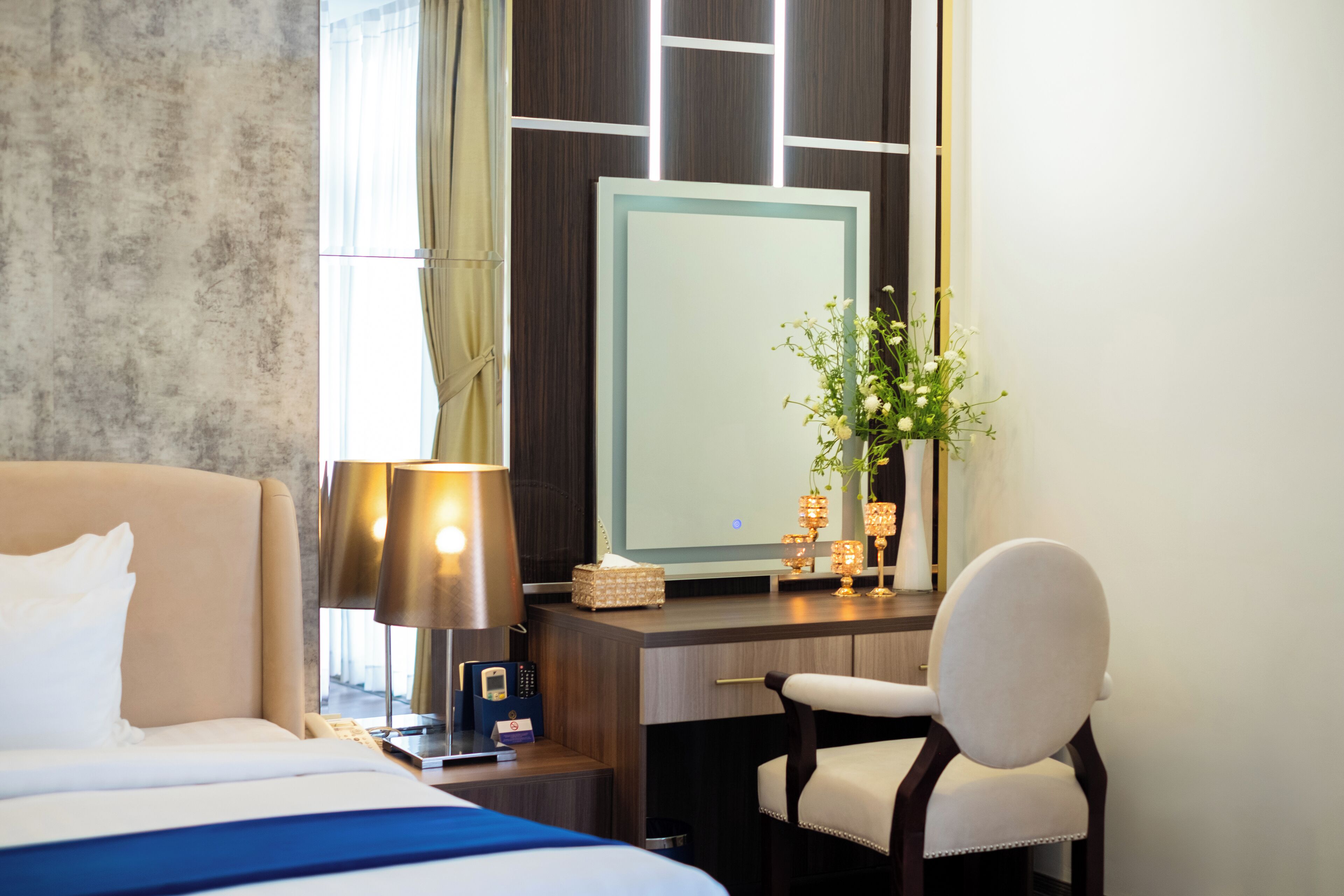 Een hotelkamer met een bed, een bureau, een stoel, een lamp, een spiegel en een vaas met bloemen.