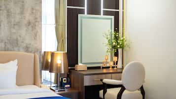 Een hotelkamer met een bed, een bureau, een stoel, een lamp, een spiegel en een vaas met bloemen.