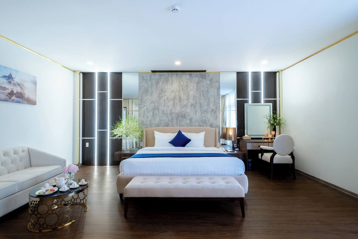 A modern bedroom with a large bed, a bedside desk, a chair, and a sofa.