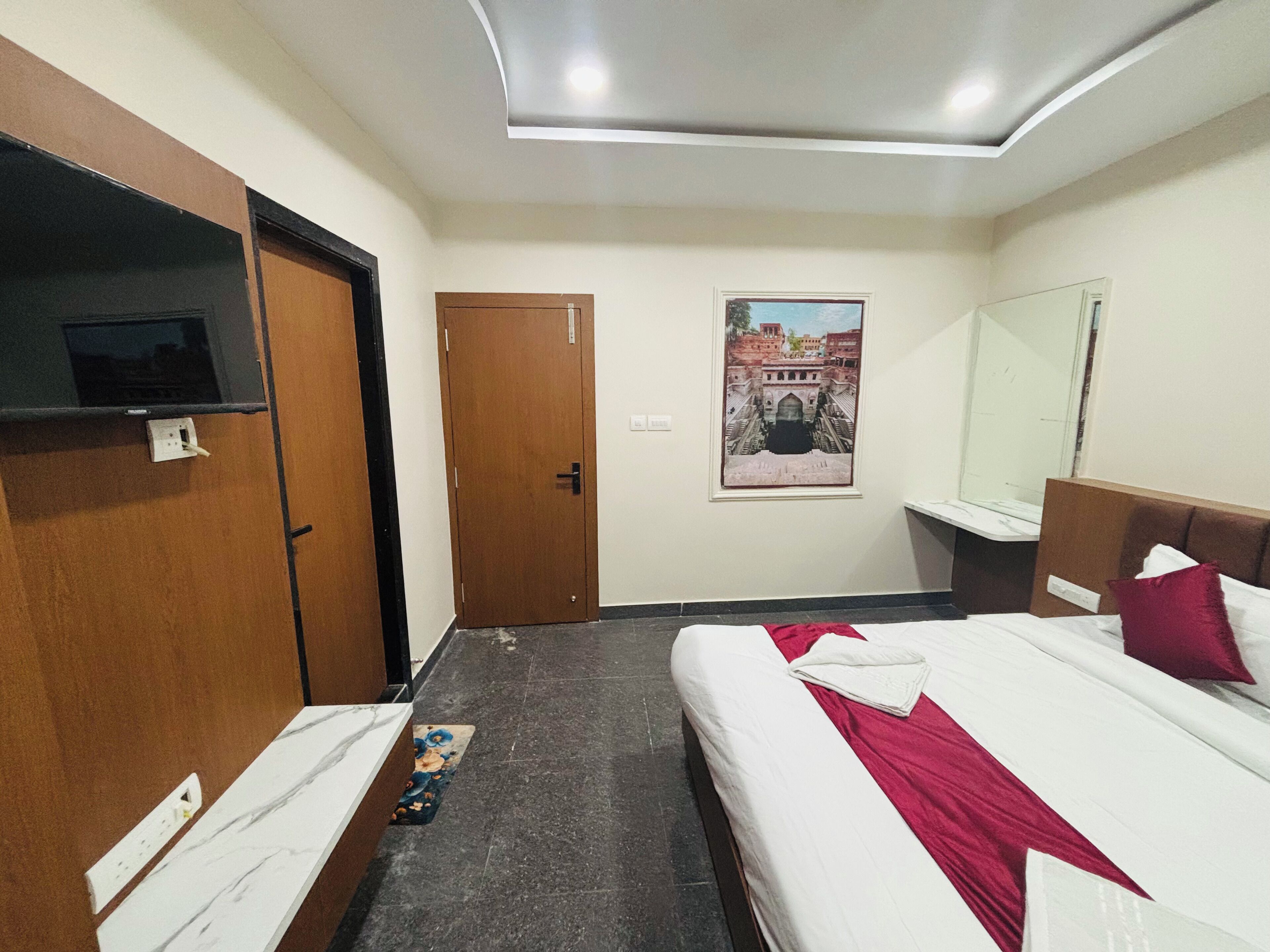A hotel room with two beds, a television, a door, a wall-mounted picture, and a mirror.
