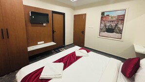 Habitación de hotel con cama, televisor montado en la pared, armario y un cuadro enmarcado.