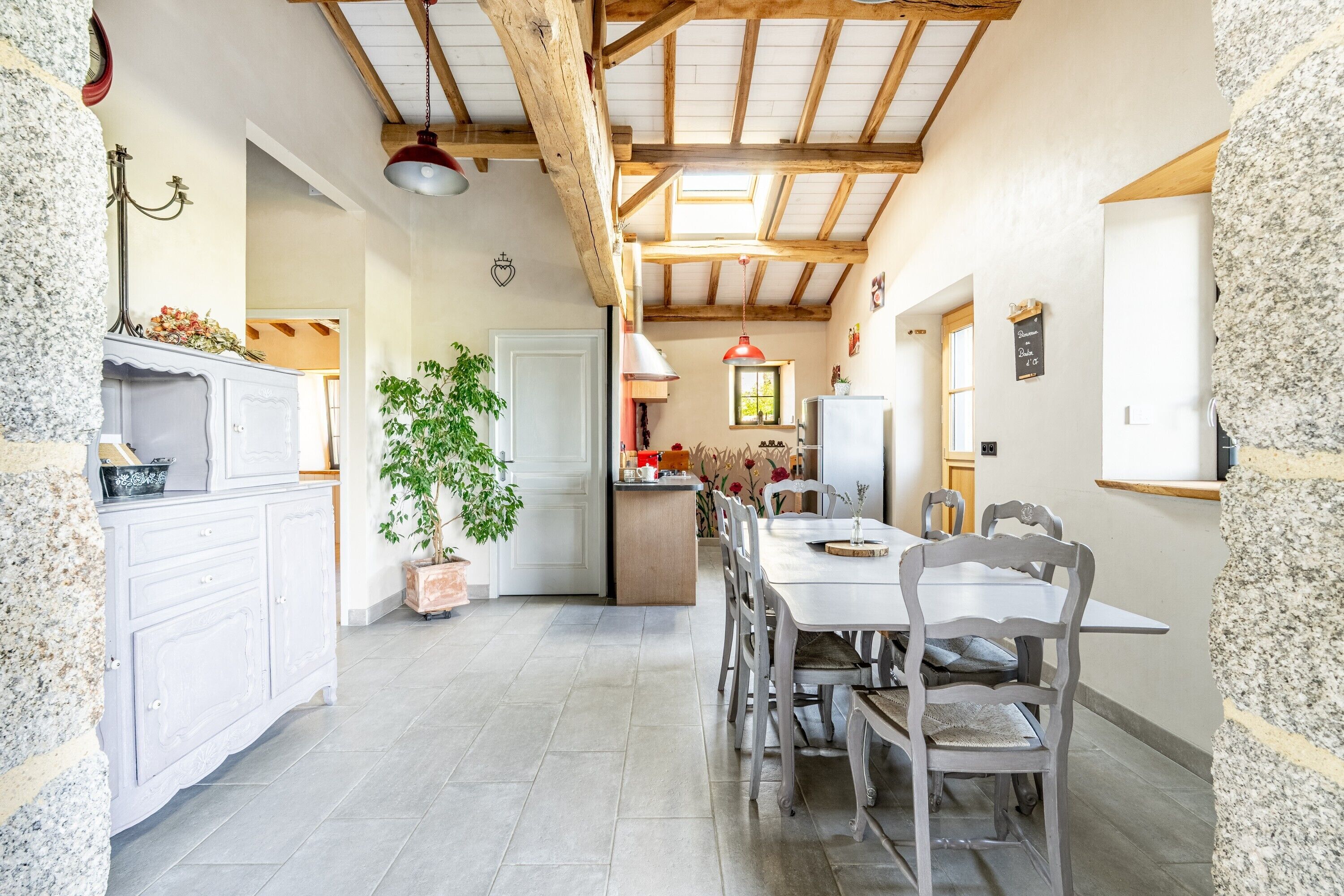A rustic kitchen with a dining area, stone walls, wooden beams, and a potted plant.