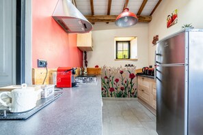 A kitchen with a stainless steel refrigerator, a red coffee machine, and a window with a view of greenery.