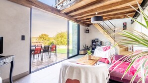 Ein modernes Interieur mit einer großen Schiebeglastür, die zu einer Außenpatio führt, einem gemütlichen Sitzbereich mit einem roten Sofa und einer Holzbalkendecke.