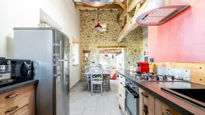 Eine Küche mit Steinwand, Holzbalken, einem Edelstahl-Kühlschrank und einem roten Backofen.