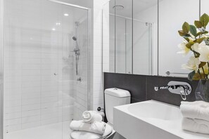 A modern bathroom with a glass shower enclosure, a white sink, and a toilet.