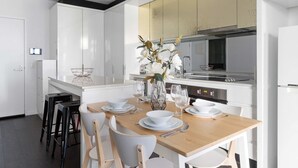 Una cocina moderna con armarios blancos, una mesa de comedor de madera dispuesta con platos, tazones y vasos blancos, y un jarrón con flores.