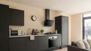 Une cuisine moderne avec des meubles de couleur sombre, un four à micro-ondes, une bouilloire et une horloge au mur.
