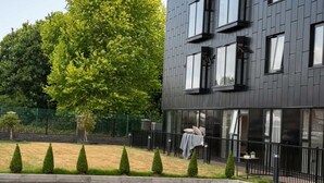 Un bâtiment moderne à la façade sombre, doté de grandes fenêtres et d’une pelouse bien entretenue, agrémentée d’arbustes taillés.