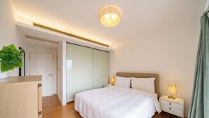 Ein modernes Schlafzimmer mit einem großen Bett, Nachttischen, einem Kleiderschrank und einer Deckenleuchte.