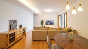 Ein modernes Wohnzimmer mit einem Holzesstisch, einem beigefarbenen Sofa und einem Flachbildfernseher.