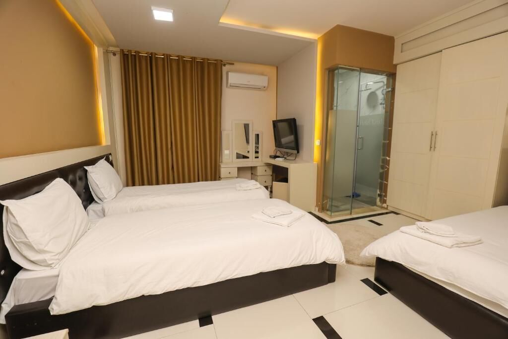 Ein Hotelzimmer mit zwei Betten, einem Fernseher, einer Duschkabine aus Glas und einem Kleiderschrank.