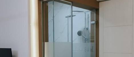 Un baño moderno con cabina de ducha de vidrio, radiador blanco y suelo de baldosas blanco y negro.