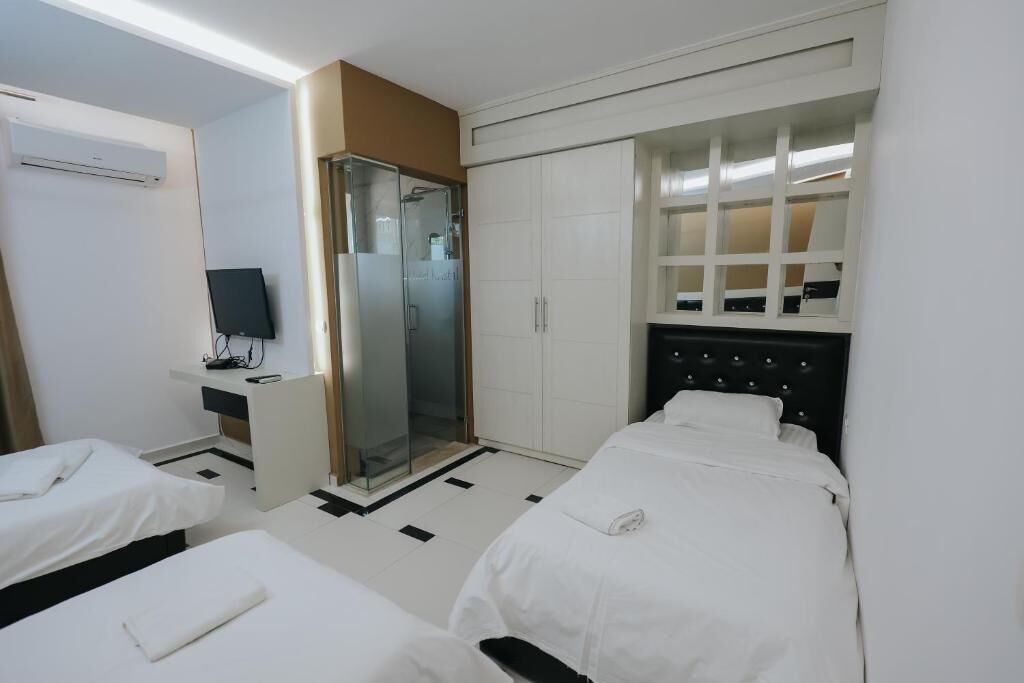 A hotel room with two beds, a shower, a wardrobe, and a television.