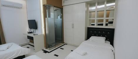 A hotel room with two beds, a shower, a wardrobe, and a television.