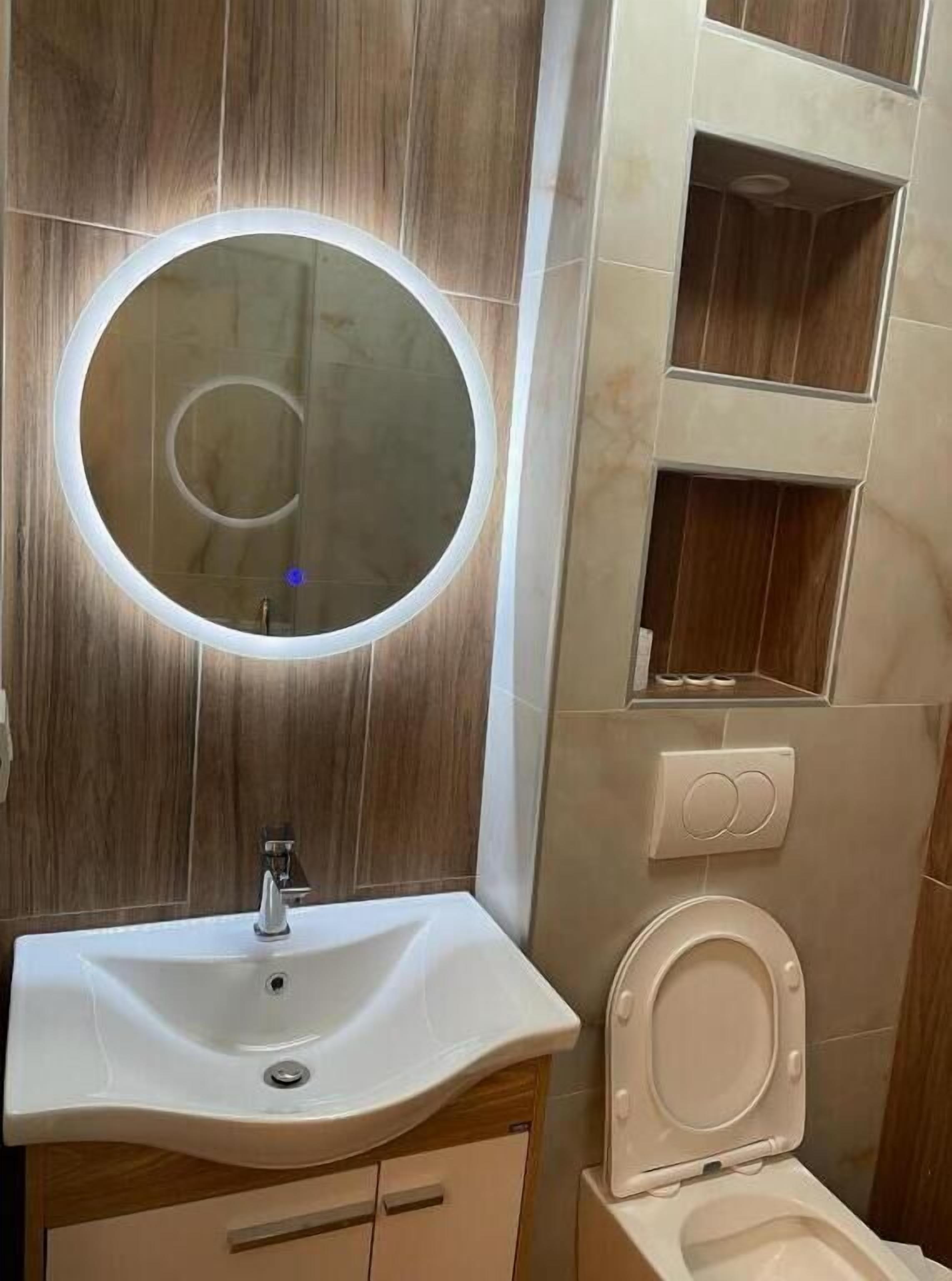 A bathroom with a round mirror, a sink, and a toilet.