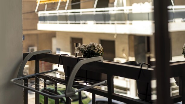 A dining area with a table set for two, a flower vase, and a view of a building with balconies and awnings. - Cozy 2BR Family-Friendly Pangrati (Athens)