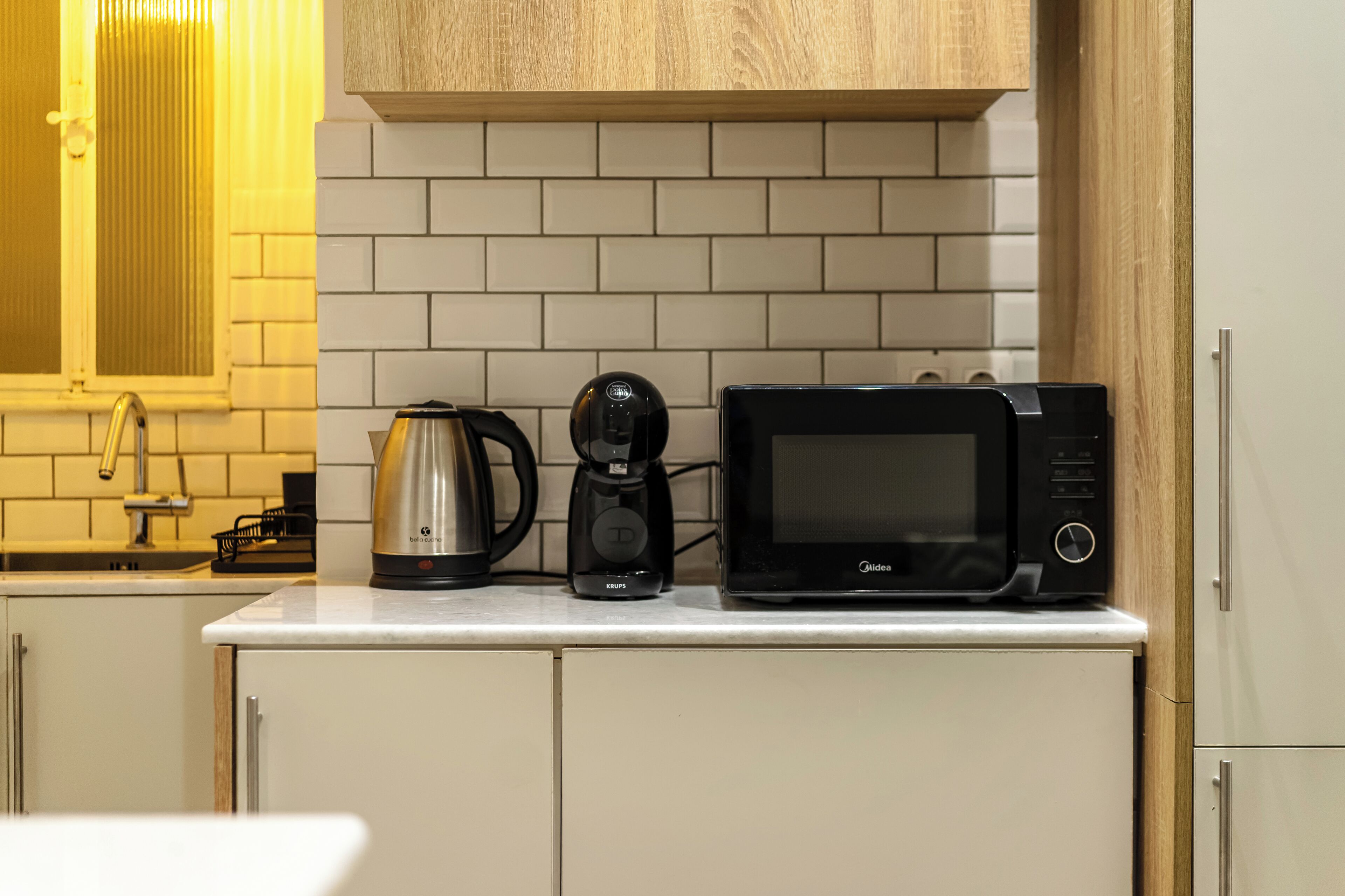 Et køkken med kaffemaskine, mikroovn og elkedel på bordet.