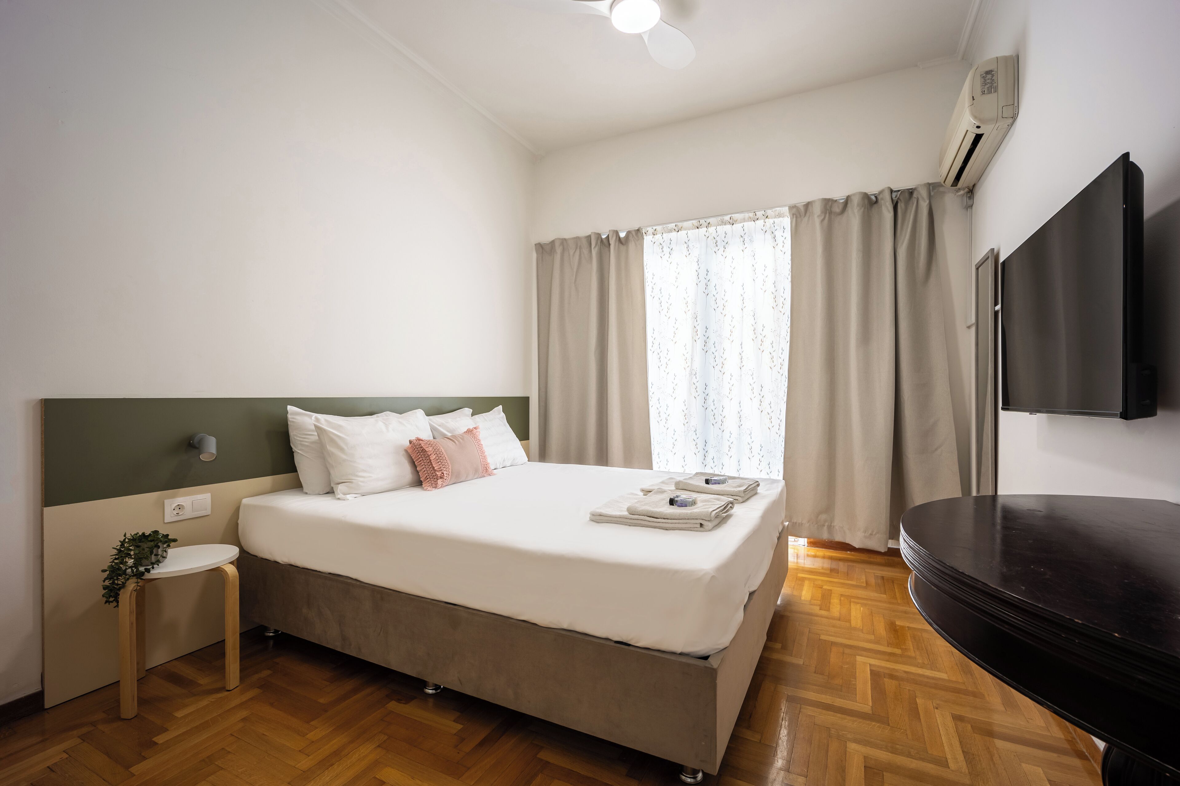 A hotel room with a bed, a small table, a TV, and a window with curtains.
