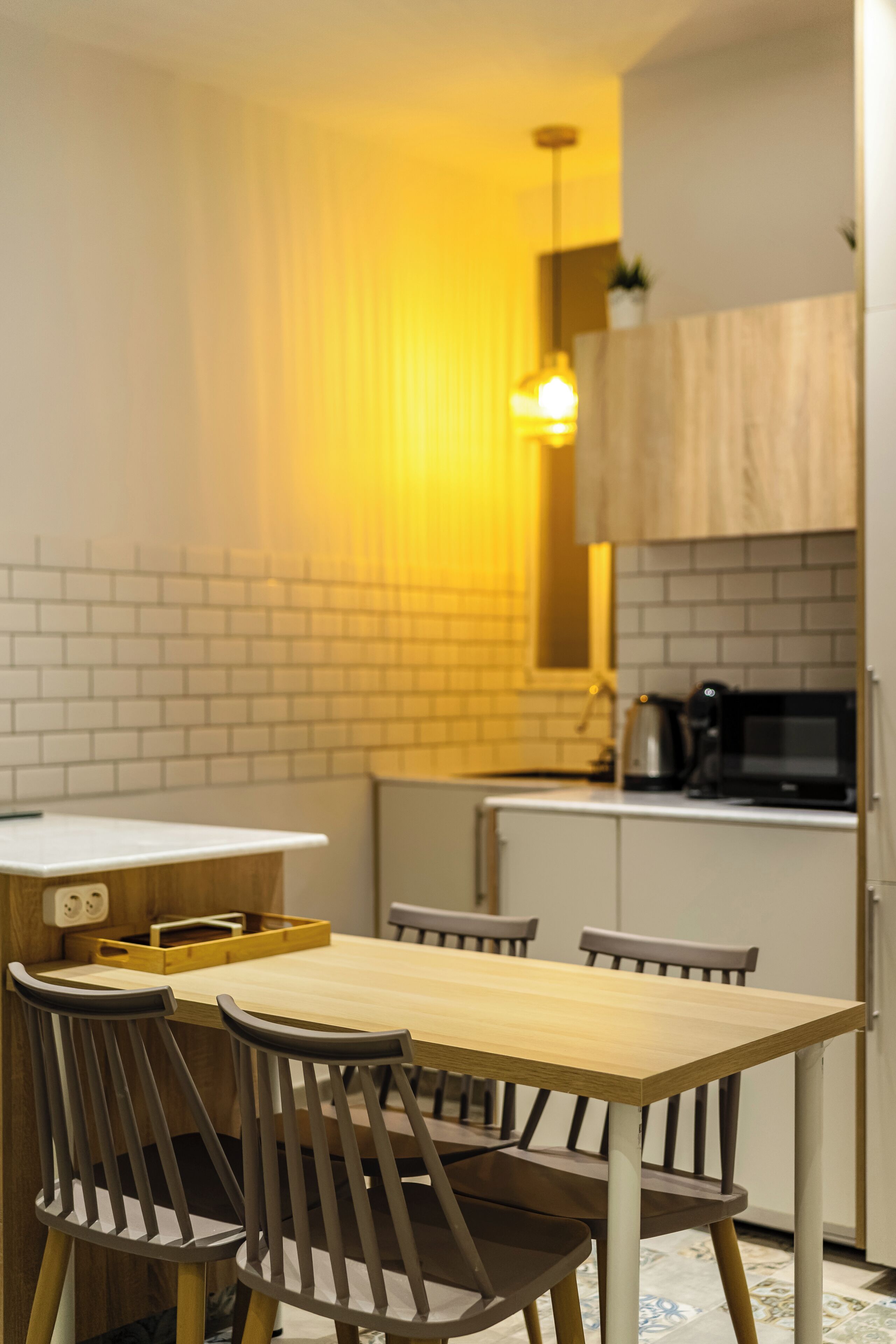 A modern kitchen with a wooden table and chairs, a hanging light fixture, and a microwave.