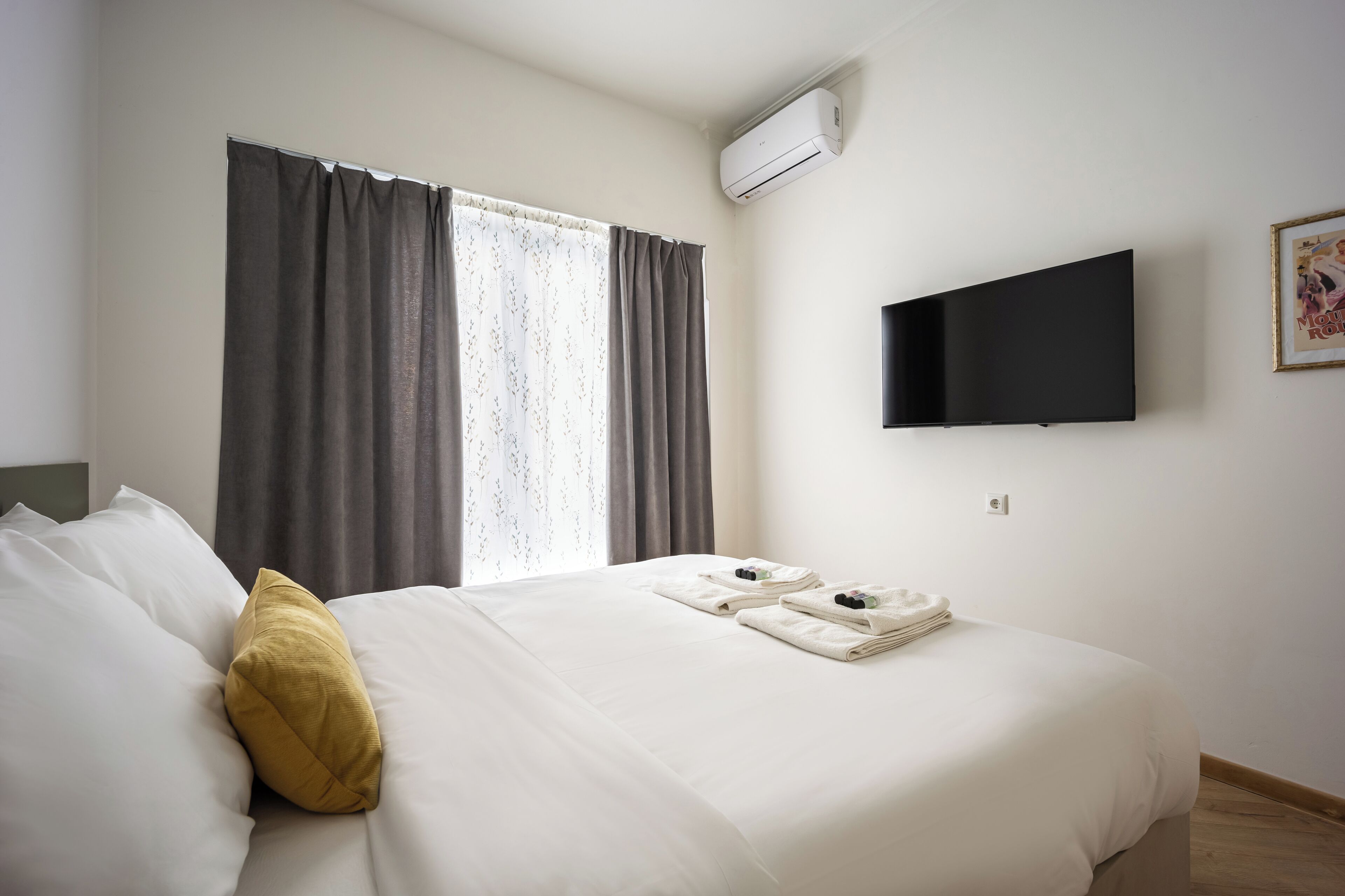 Habitación de hotel con cama, televisor en la pared y ventana con cortinas.