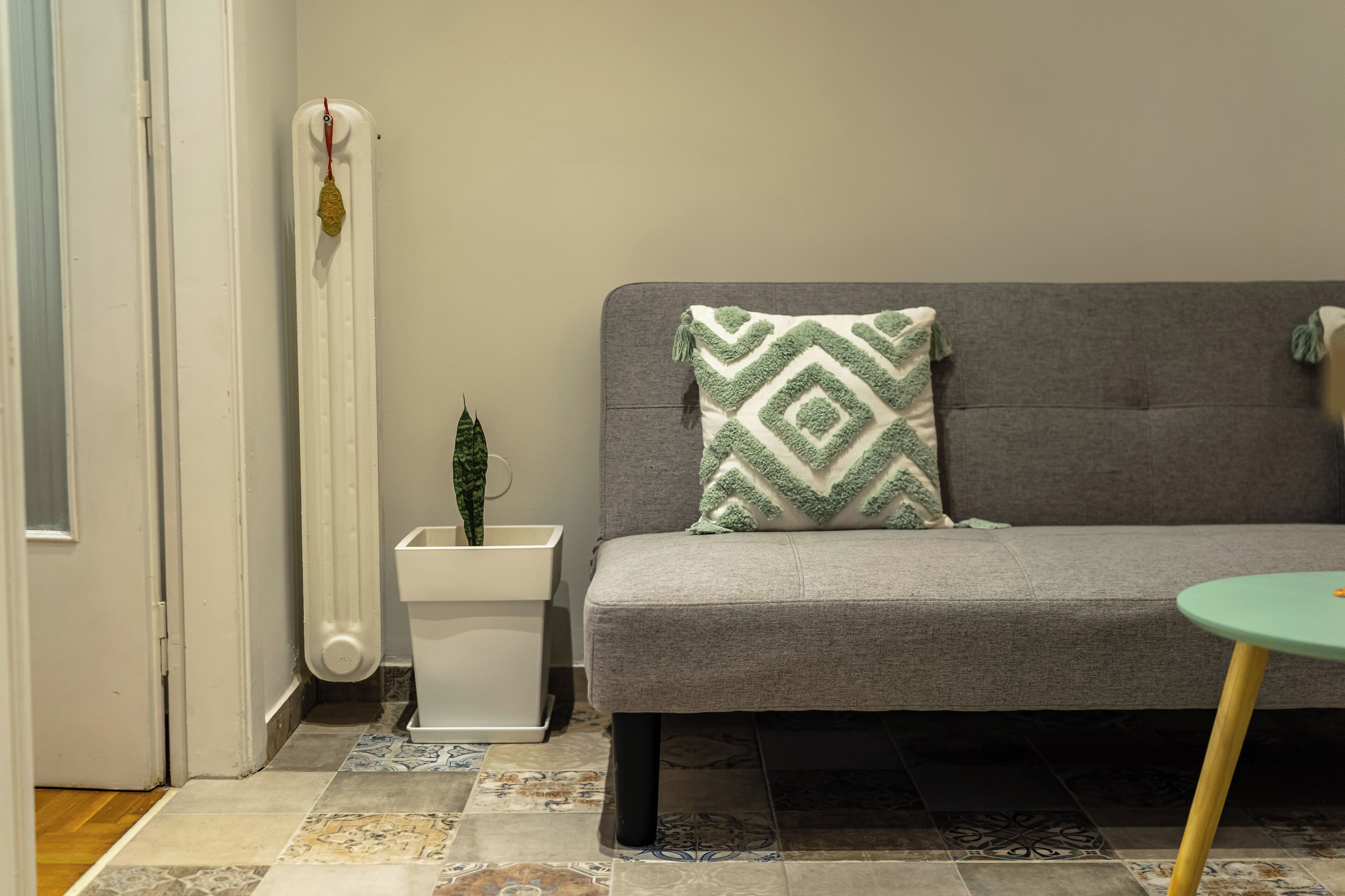 A modern living room with a grey sofa, a patterned throw pillow, a small green plant, and a white radiator.