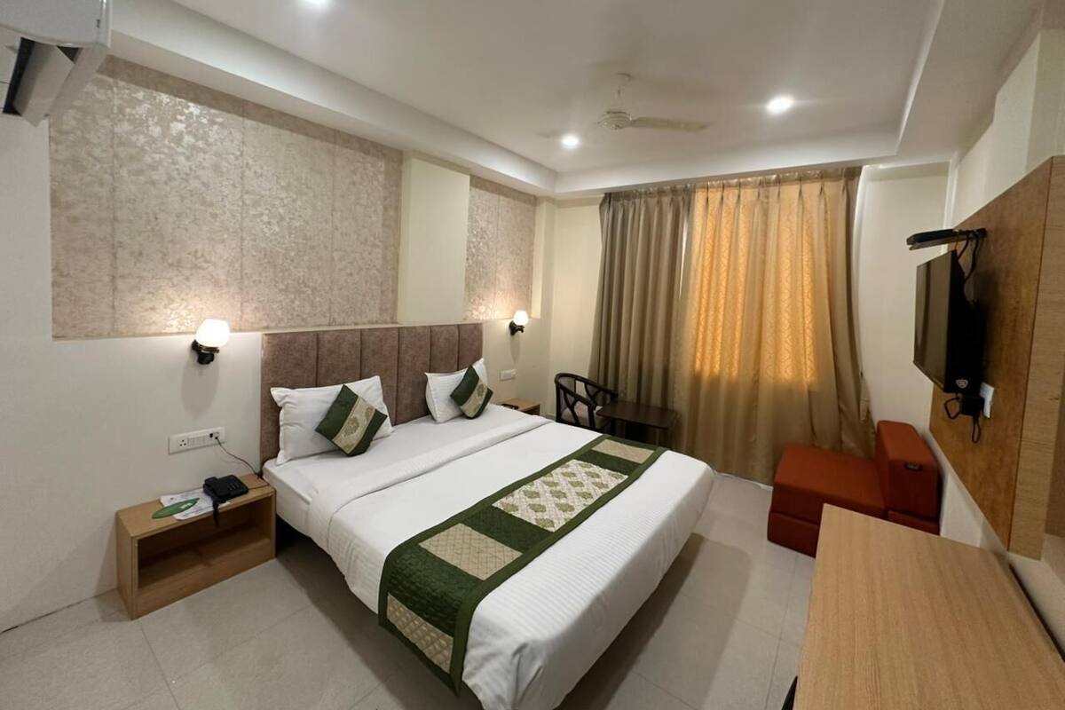 Une chambre d’hôtel avec un grand lit, des tables de chevet, un bureau, une chaise, un téléviseur fixé au mur et un ventilateur de plafond.