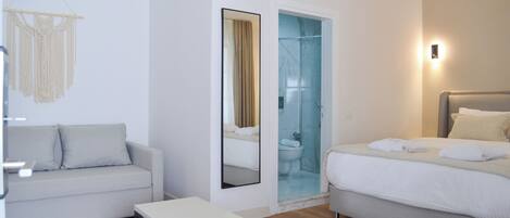 Habitación de hotel moderna con sofá, cama, una mesita y zona de ducha con cristal.