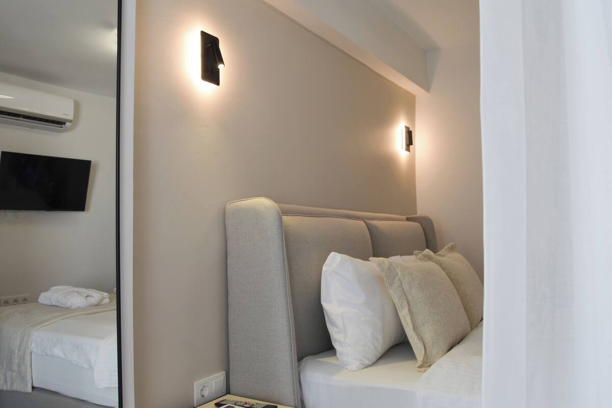 A modern hotel room with a bed, a television mounted on the wall, and a wall-mounted air conditioner.