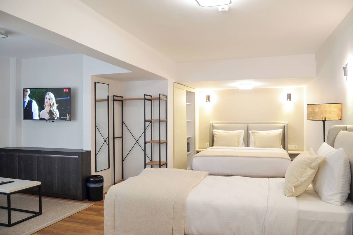 A modern hotel room with a large bed, a TV mounted on the wall, a desk, and a walk-in closet.