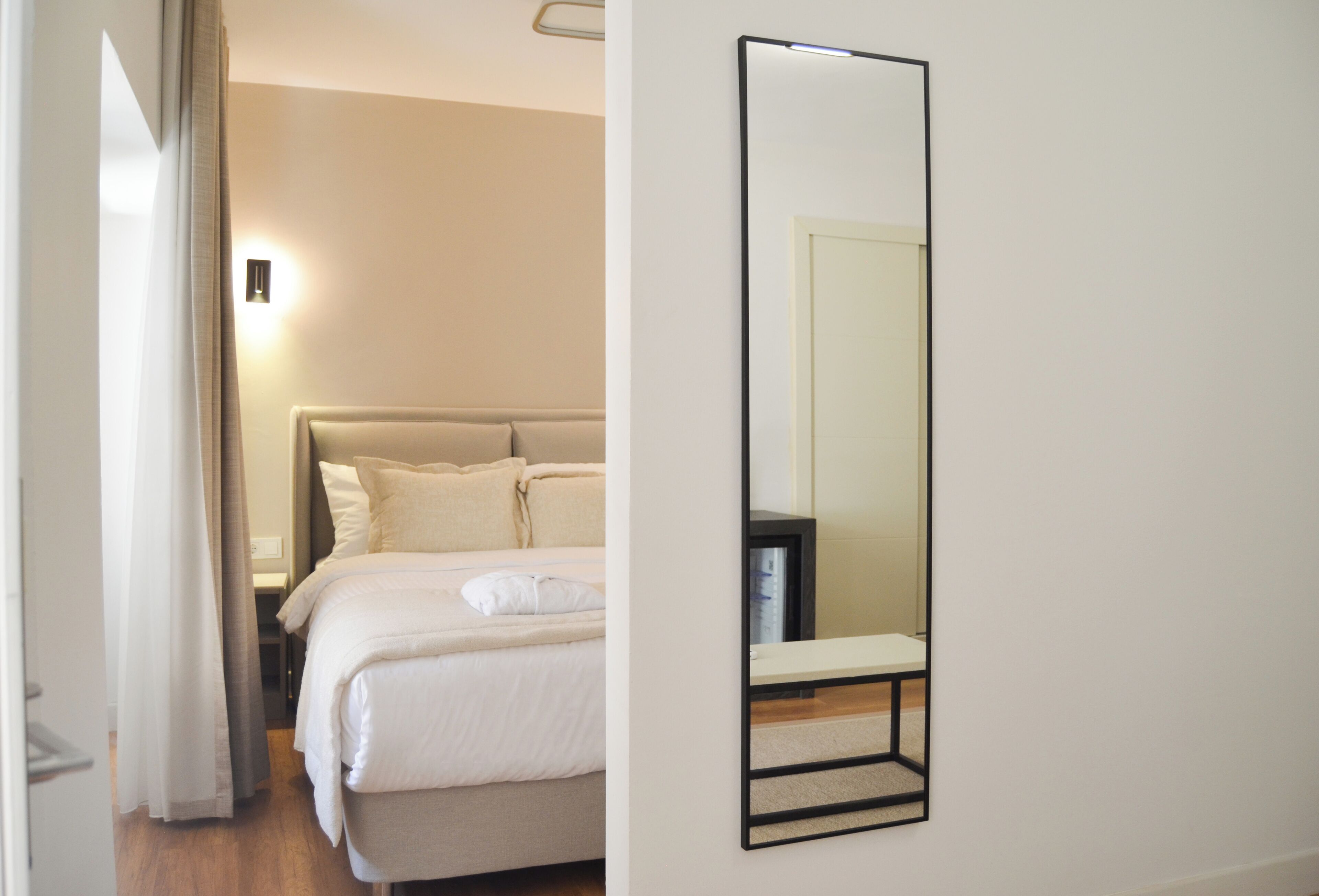 Un dormitorio con cama, mesita de noche, espejo y lámpara de pared.