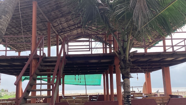 Ein Gebäude am Strand mit einer Holztreppe, einem Strohdach und Blick auf das Meer.