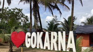 Ein Schild mit dem Wort "GOKARNA" und einem roten Herzsymbol, umgeben von Palmen und einer Sandfläche.