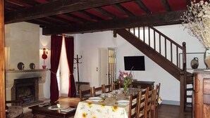 A dining area with a wooden table set for four, a fireplace, and a staircase leading to an upper level. - Haven of peace: 8-person gîte with swimming pool in Boisse (Boisse)