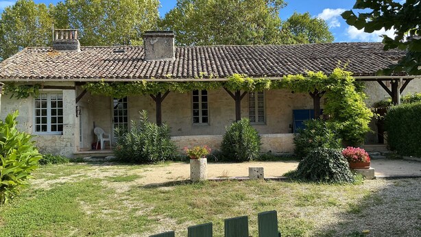 A rustic stone building with a tiled roof, a covered porch, and a garden with various plants and a gravel path. - Haven of peace: 8-person gîte with swimming pool in Boisse (Boisse)