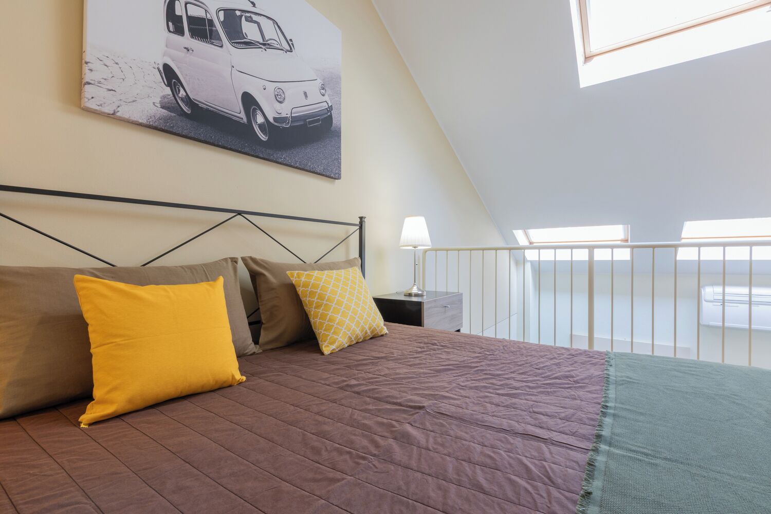 Ein Schlafzimmer mit Bett, Kissen, einem Nachttisch, einer Lampe und einem Fenster mit Blick.