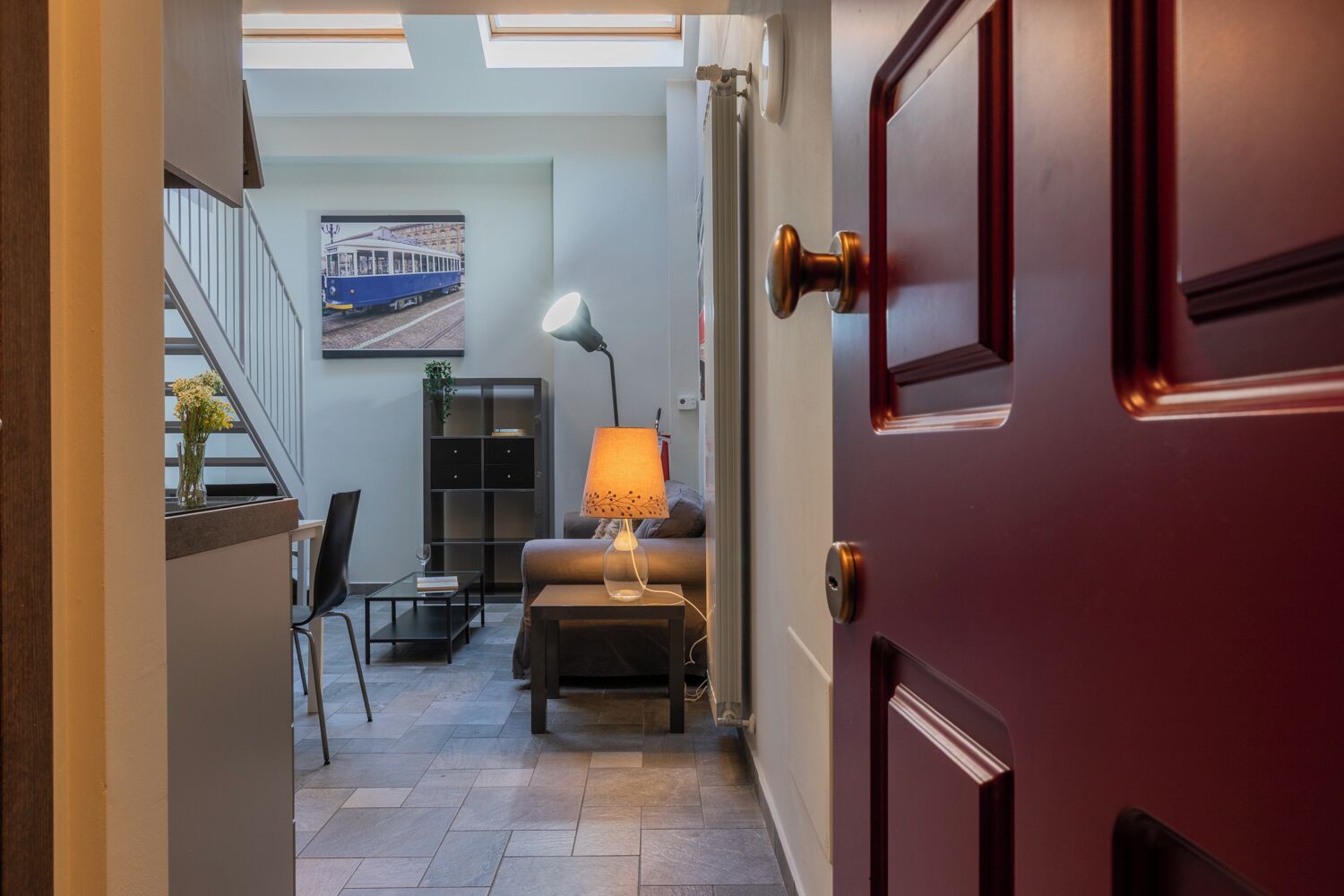 A hallway leading to a living area with a sofa, a lamp, and a coffee table. A staircase is visible in the background.