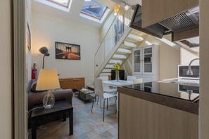 A compact kitchen with a dining area, a staircase, and a living room with a sofa and lamp. - Grossi Turin Lofts by Wonderful Italy (Turin)