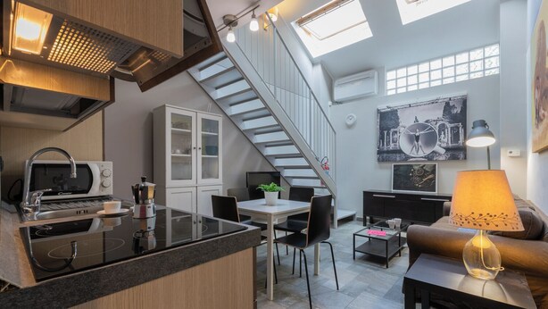A modern kitchen with a built-in microwave, a coffee maker, and a dining area with a table and chairs. There is a staircase leading to an upper level. - Grossi Turin Lofts by Wonderful Italy (Turin)