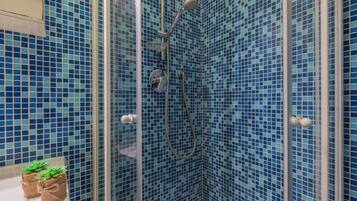 Ducha con azulejos de mosaico azules, puerta de cristal y una planta pequeña en la encimera.