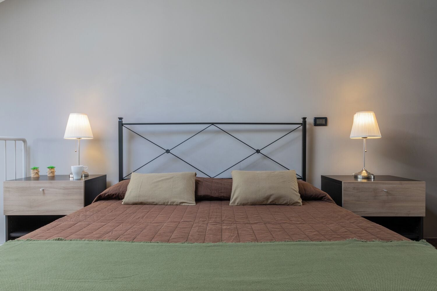 A neatly made bed with a wooden headboard, two bedside tables with lamps, and a green throw blanket.