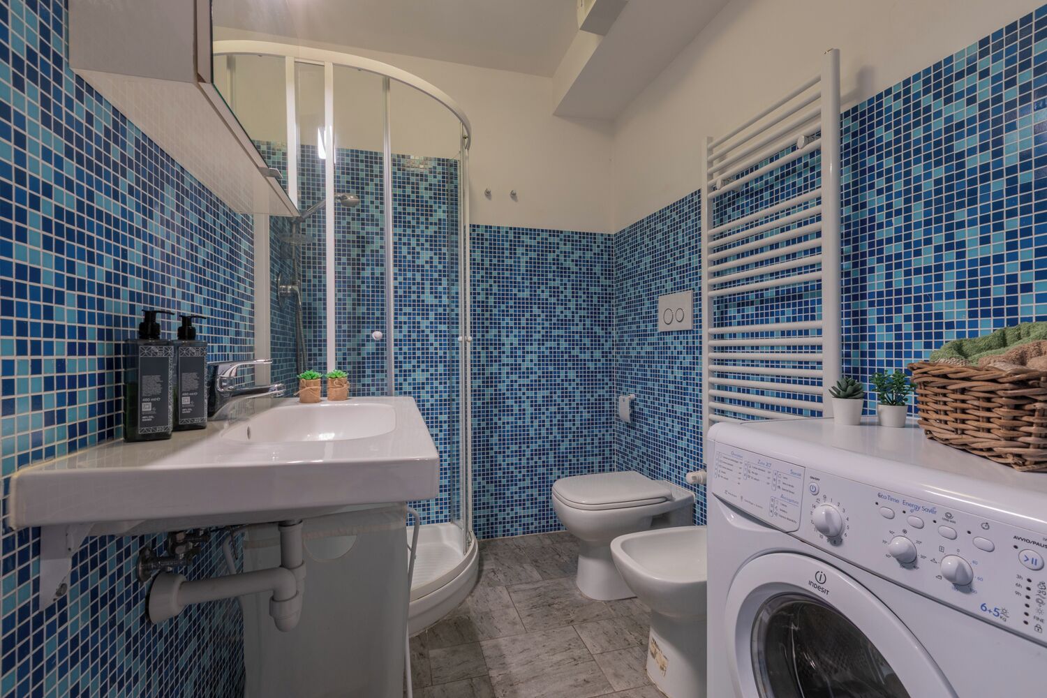 A bathroom with a sink, toilet, shower, and washing machine.
