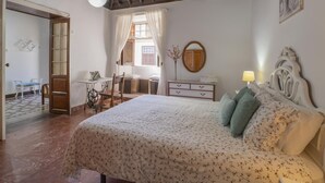 A bedroom with a bed, a desk, a chair, a dresser, and a window with curtains.