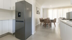 Una cocina moderna con un refrigerador de acero inoxidable, gabinetes blancos, un comedor con mesa y sillas, y un televisor sobre una encimera.