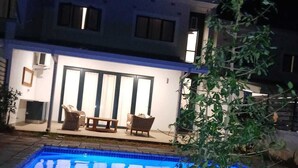 Una piscina con un patio, mobiliario de exterior y una casa al fondo.