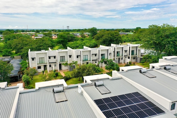 A modern building with multiple units, solar panels on the roof, and a green landscape in the background.