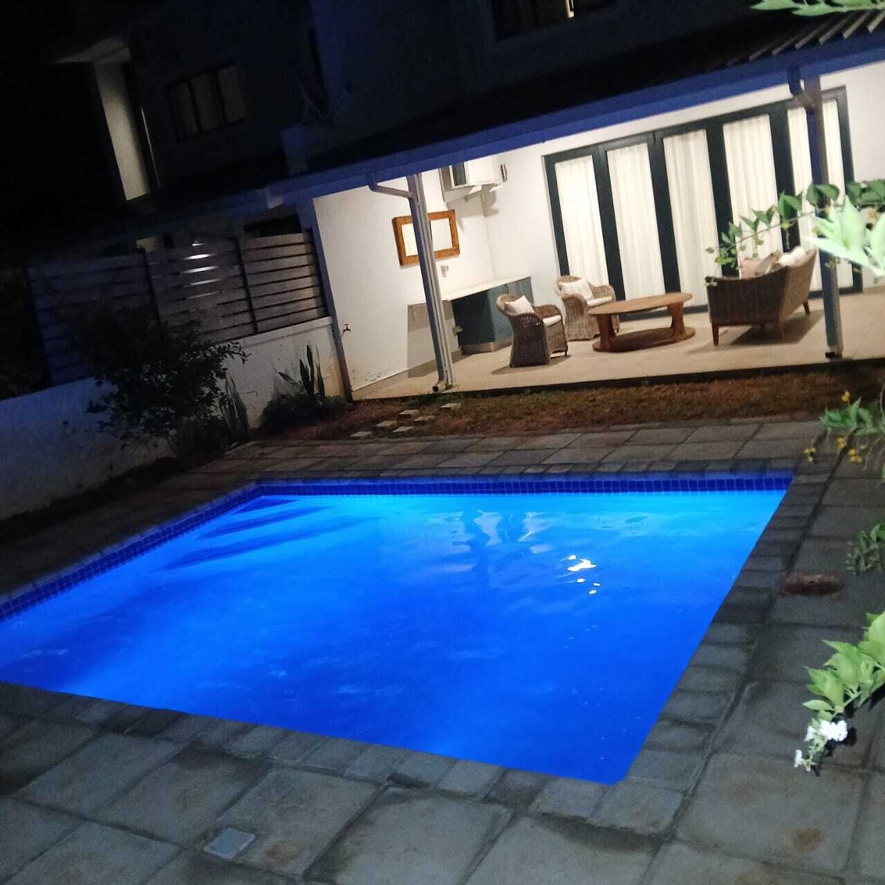A swimming pool with a tiled edge, a patio area with outdoor furniture, and a building with large windows in the background.